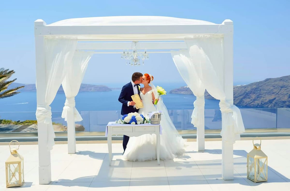 Wedding ceremony under white gazebo with caldera view