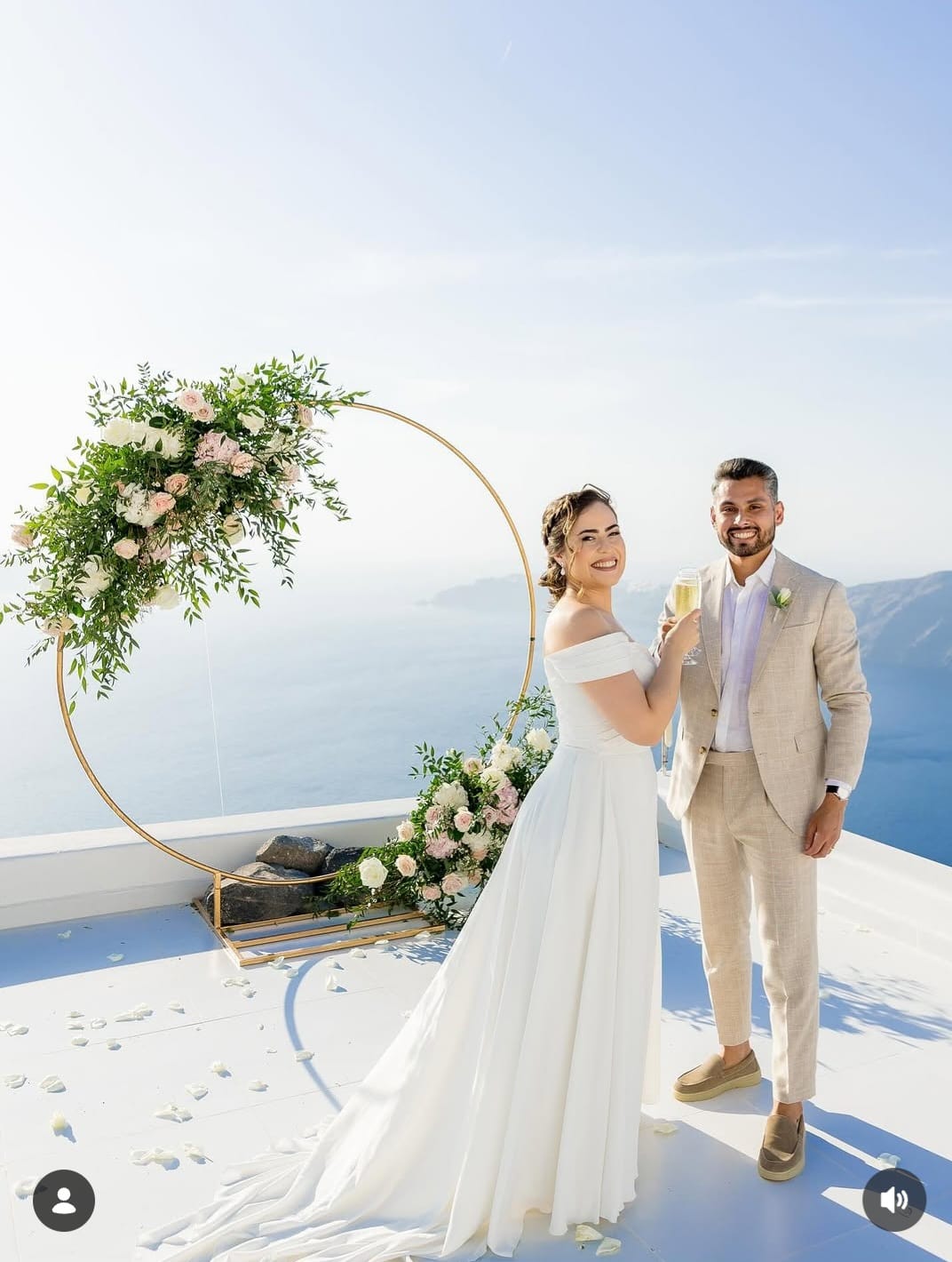 Couple celebrating at circular floral arch with caldera backdrop