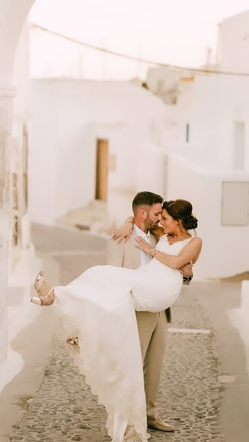 Groom carrying bride through Santorini village streets